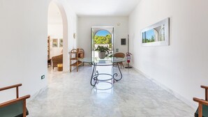 Un hall d’entrée spacieux, avec une table et des chaises en verre, un extincteur et un tableau encadré au mur.