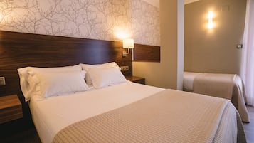 Quarto de hotel com uma cama grande, uma cama menor e uma mesa de cabeceira com abajur.