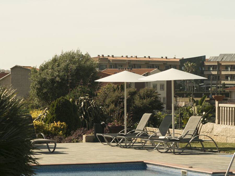 A swimming pool with lounge chairs and umbrellas, surrounded by greenery and buildings.