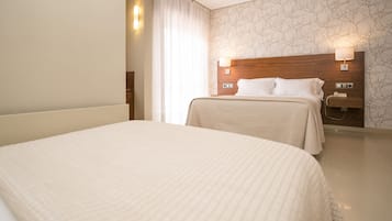 A hotel room with two beds, a wooden headboard, a nightstand with a lamp, and a wall with a tree pattern.