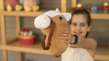 Un enfant tenant un jouet représentant une tête de cheval devant une étagère remplie de divers jouets et un panneau indiquant « BIENVENUE ».