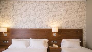 Habitación de hotel con dos camas, cabeceros de madera, una pared con diseño de ramas de árbol y lámparas de noche.