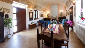 A dining area with a long wooden table, chairs, and a decorative runner. There are potted plants and wall-mounted lighting fixtures. - Villa Teresa (Ugento)