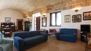A living room with a stone ceiling, two blue sofas, a television, and framed pictures on the wall. - Villa Teresa (Ugento)