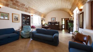 A spacious living room with a high arched ceiling, a blue sofa, a striped armchair, and a brown leather chair. - Villa Teresa (Ugento)