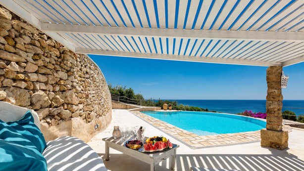 Un muro de piedra, una piscina y una mesa con comida y bebidas.