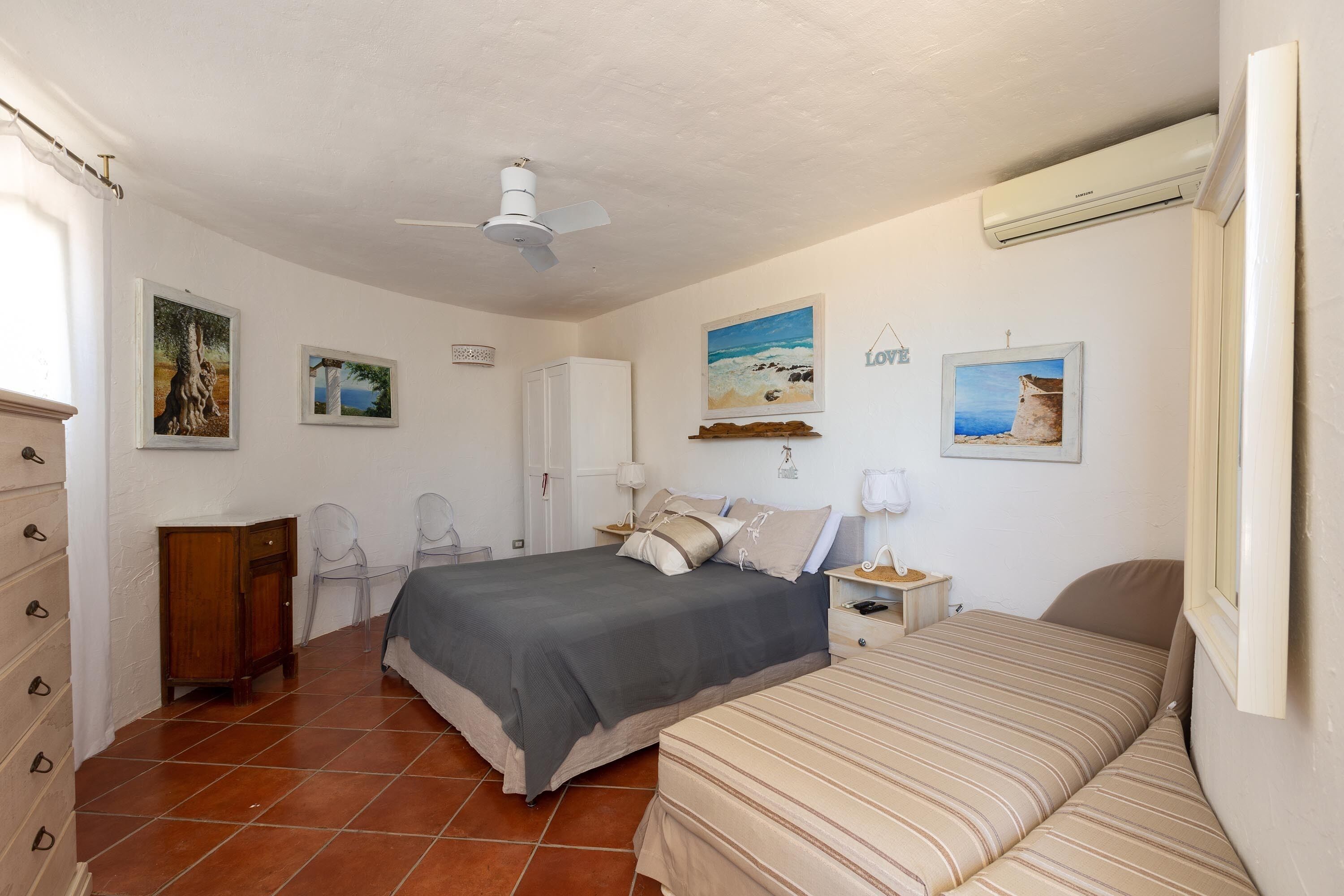A bedroom with two beds, a ceiling fan, an air conditioner, and several framed pictures on the walls.