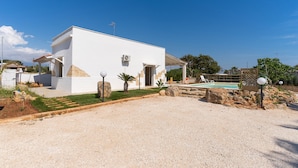 A modern white building with a pool, surrounded by a gravel driveway and a small garden area. - Villetta Marcella (Racale)