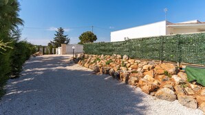 A gravel driveway leading to a white building with a green hedge and a stone wall. - Villetta Marcella (Racale)