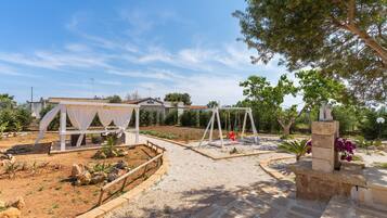 Relax in a serene garden setting with a swing, surrounded by lush plants and a shaded pergola.