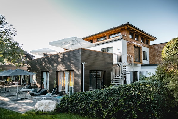 A modern two-story house with a wooden deck, outdoor seating, and a spiral staircase. - Hotel Stroblerhof (Strobl)