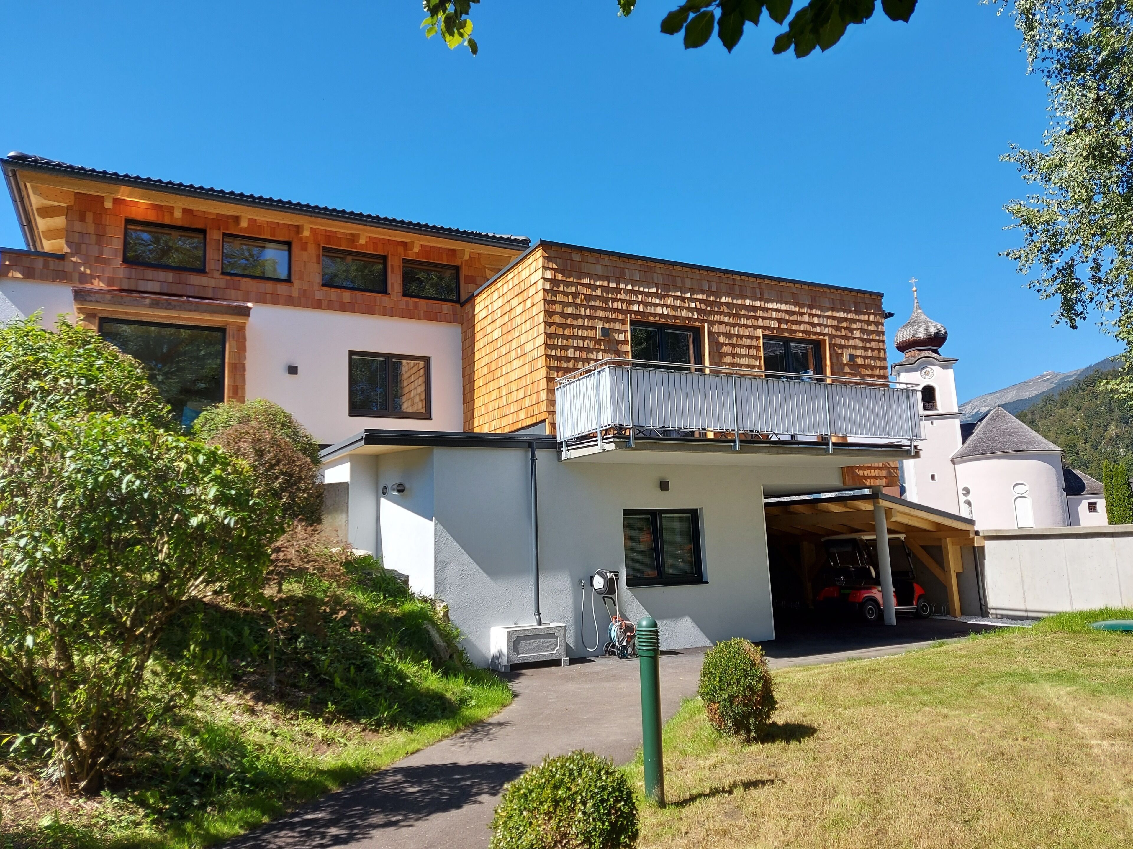 Una casa moderna con un garaje amplio, un balcón y una iglesia al fondo.