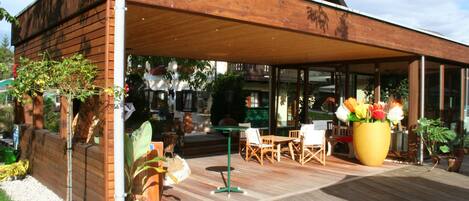 Un patio al aire libre con piso de madera, una zona de estar techada y plantas en macetas.