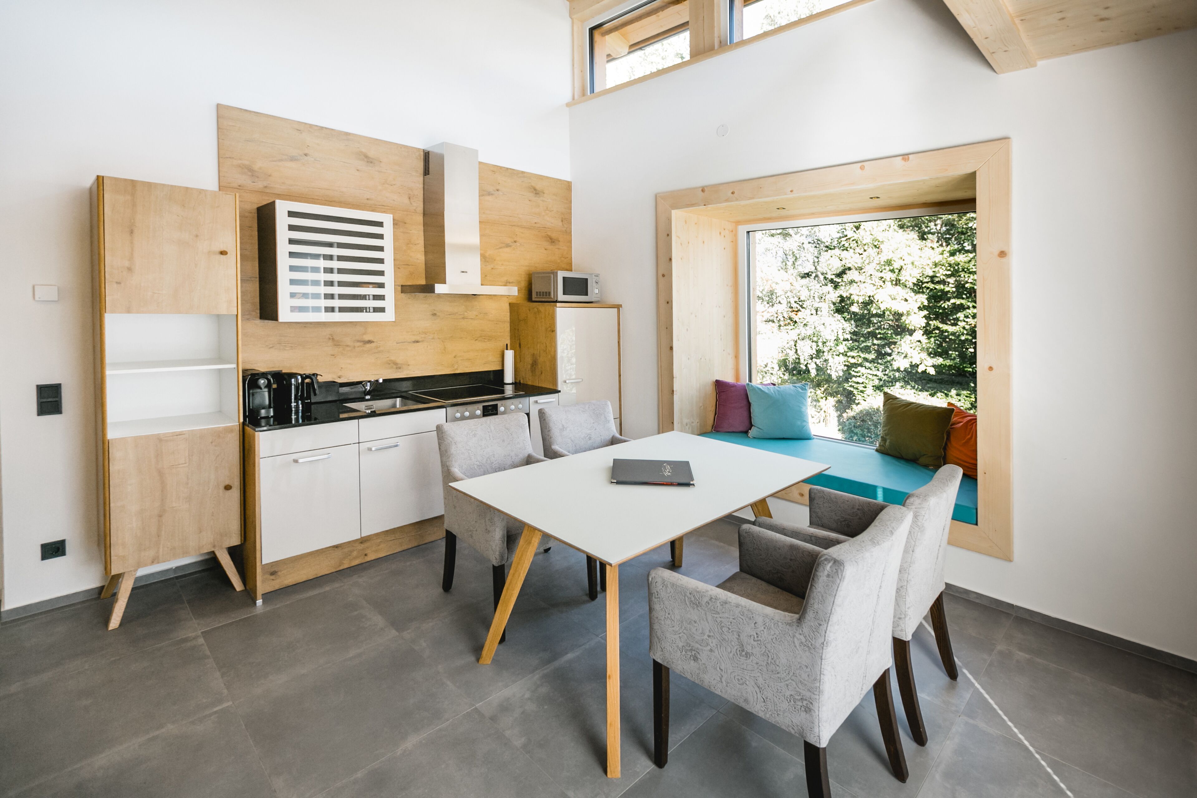 Una cocina moderna con comedor, armarios de madera y un amplio ventanal con vistas a zonas verdes.