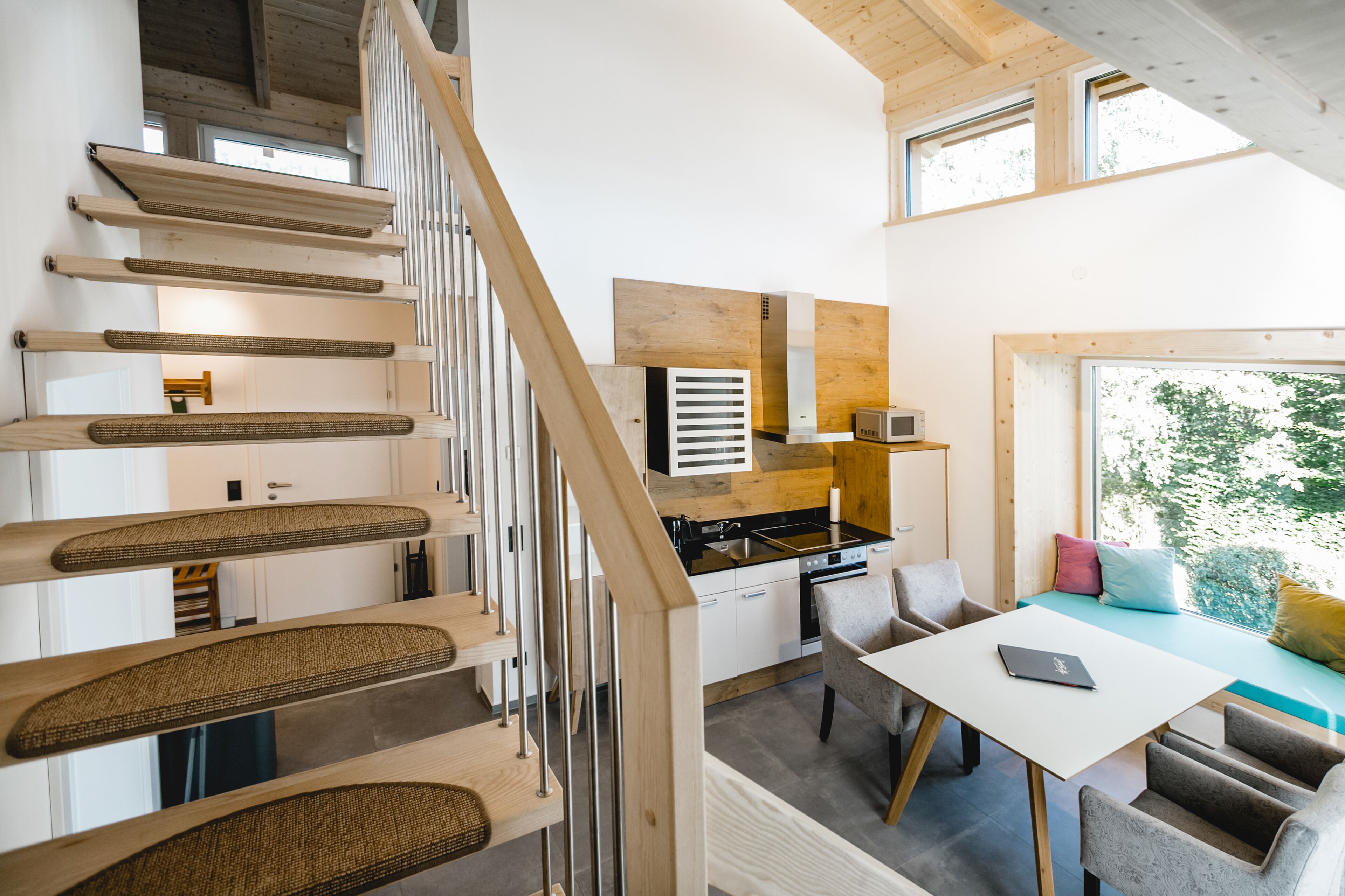 Une cuisine moderne équipée d’un four à micro-ondes, d’une cuisinière et d’un évier. On y trouve également un coin repas avec une table et des chaises. Un escalier en bois mène à un autre niveau.