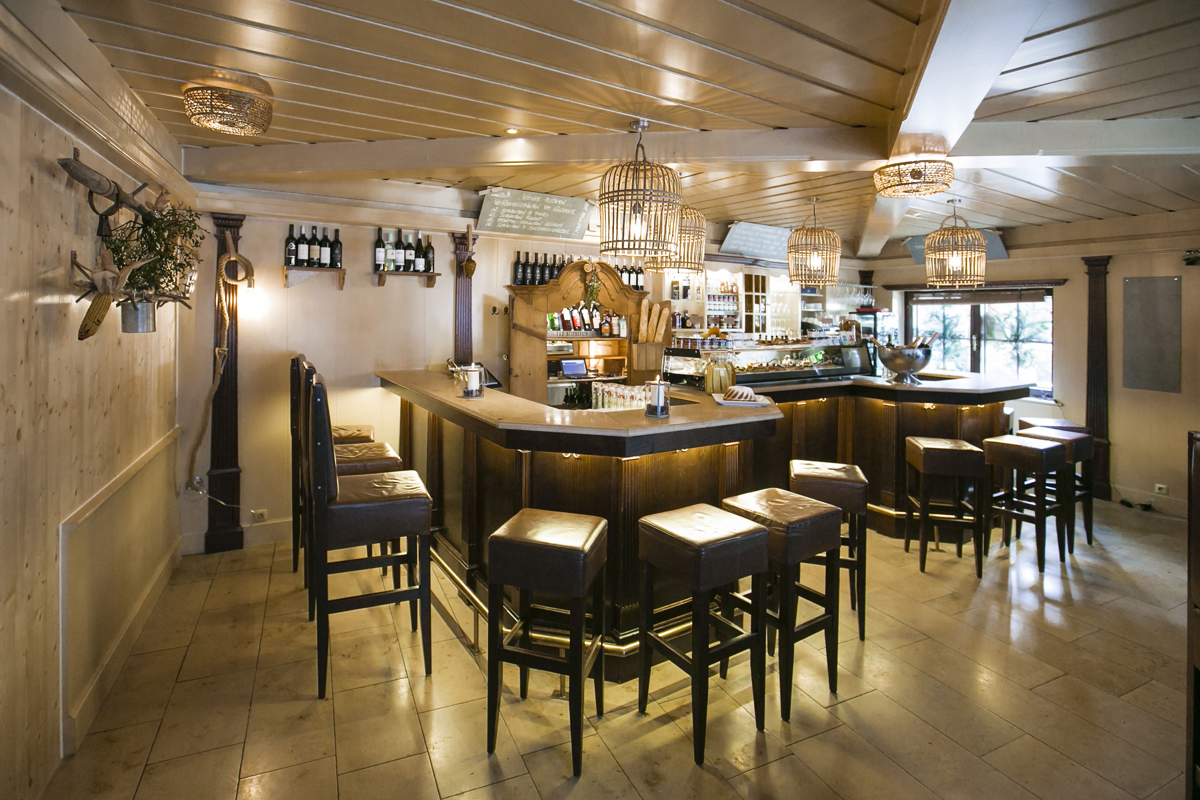 A bar area with wooden bar stools, a counter with bottles, and pendant lighting.