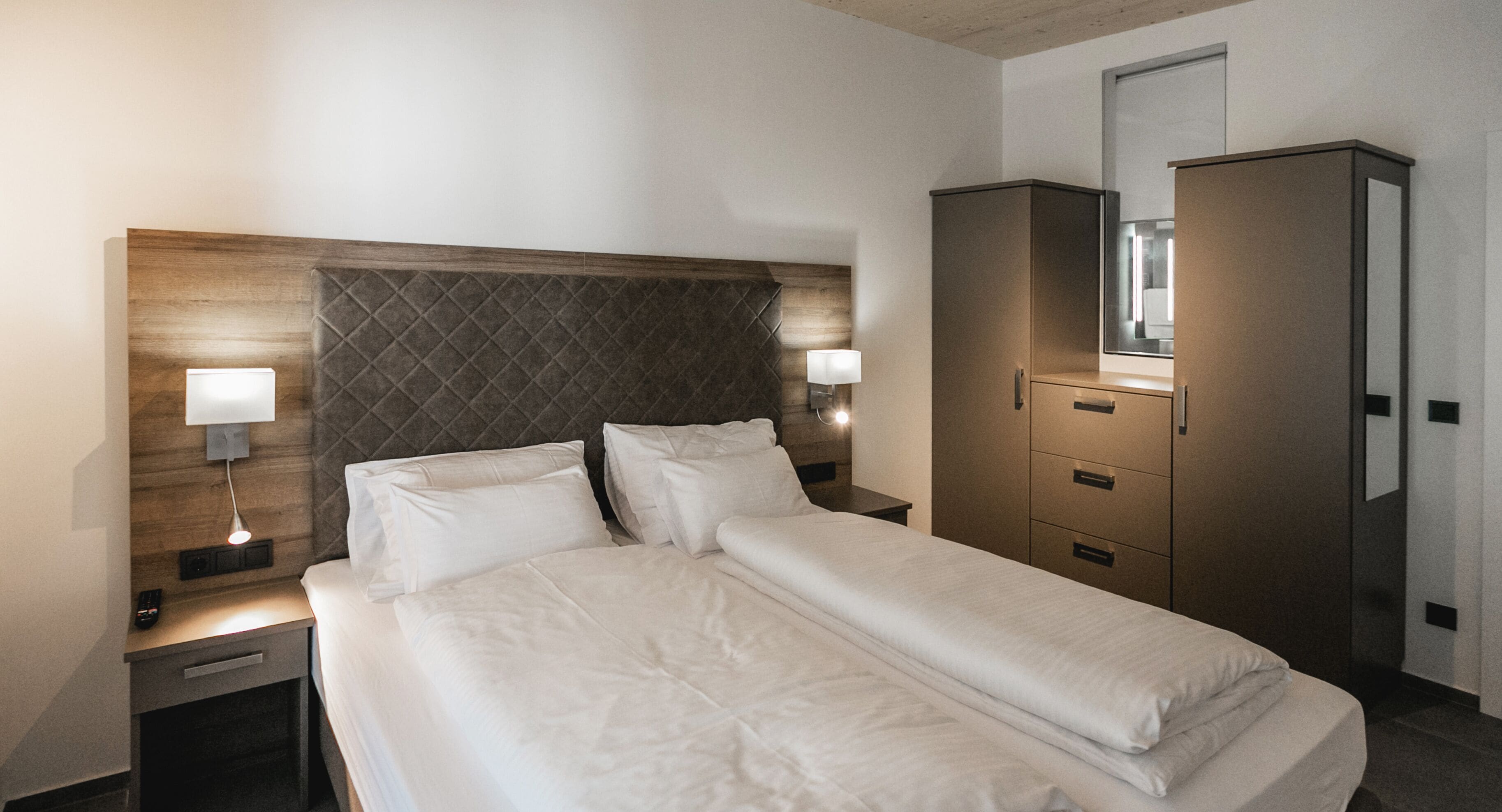 A hotel room with a bed, bedside lamps, a wardrobe, and a mirror.
