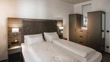 A hotel room with a bed, bedside lamps, a wardrobe, and a mirror.