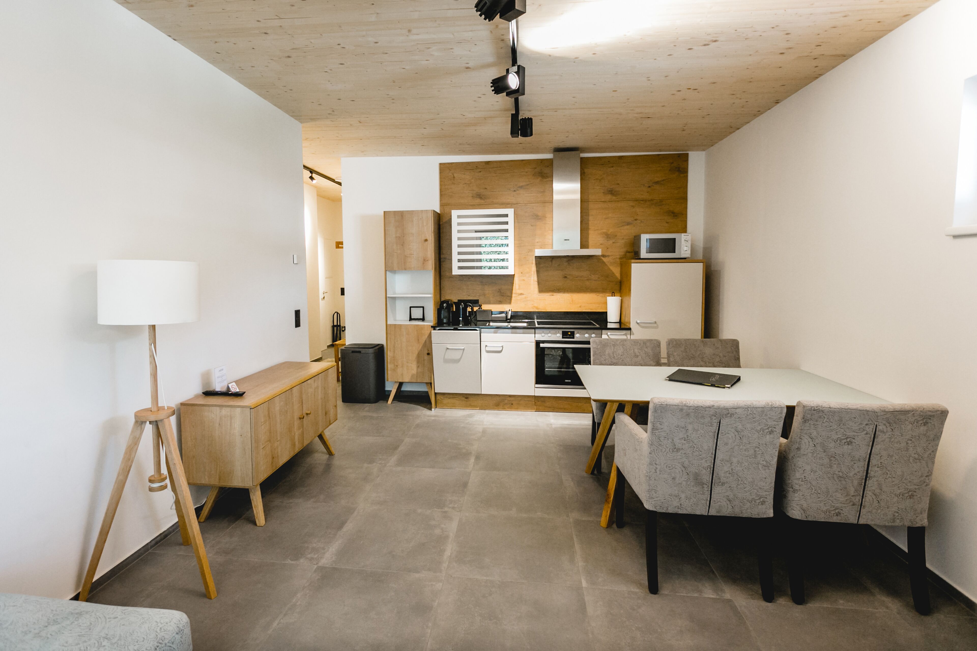 A modern kitchen with wooden cabinets, a dining area with a table and chairs, and a lamp.
