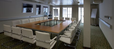 A conference room with a long table and white chairs, large windows, and a whiteboard.
