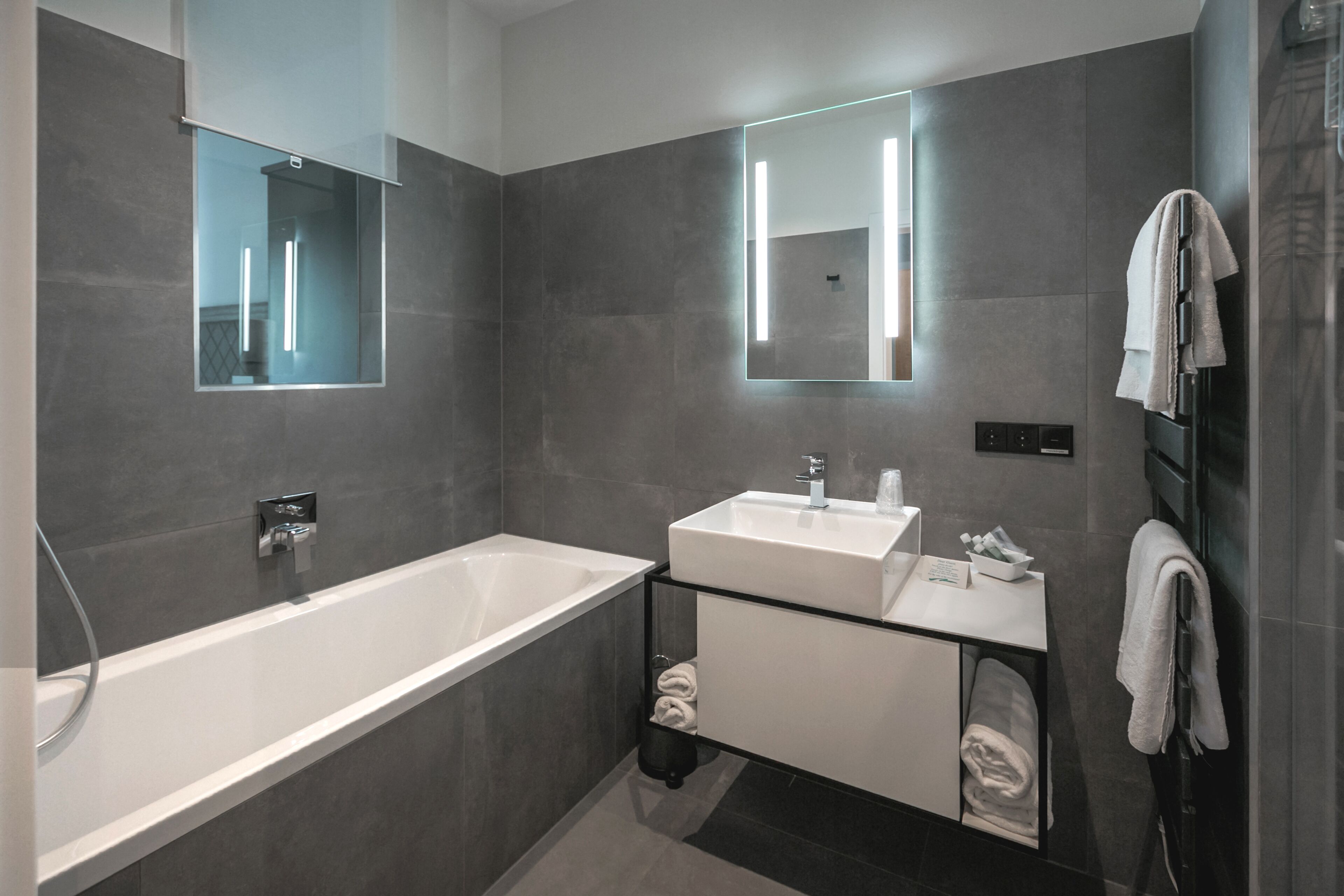 Un baño moderno con una bañera grande, dos lavamanos y un tocador con puerta de cristal.