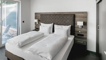 A double bed with white linens, a wooden headboard, bedside tables with lamps, and a sliding glass door to a balcony.