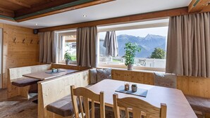 A wooden interior with a dining area, benches, and a view of mountains. - Panorama (Finkenberg)