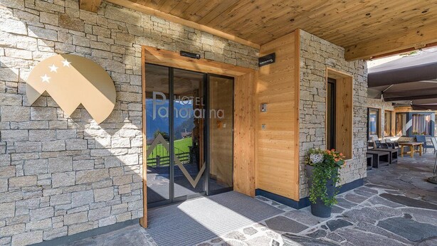 A hotel entrance with stone walls, wooden beams, and a glass door leading inside. - Panorama (Finkenberg)