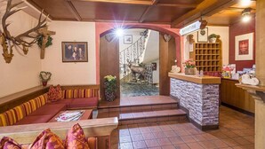 A reception area with a stone counter, a wooden reception desk, a framed photograph, and a large antler mounted on the wall. - Panorama (Finkenberg)