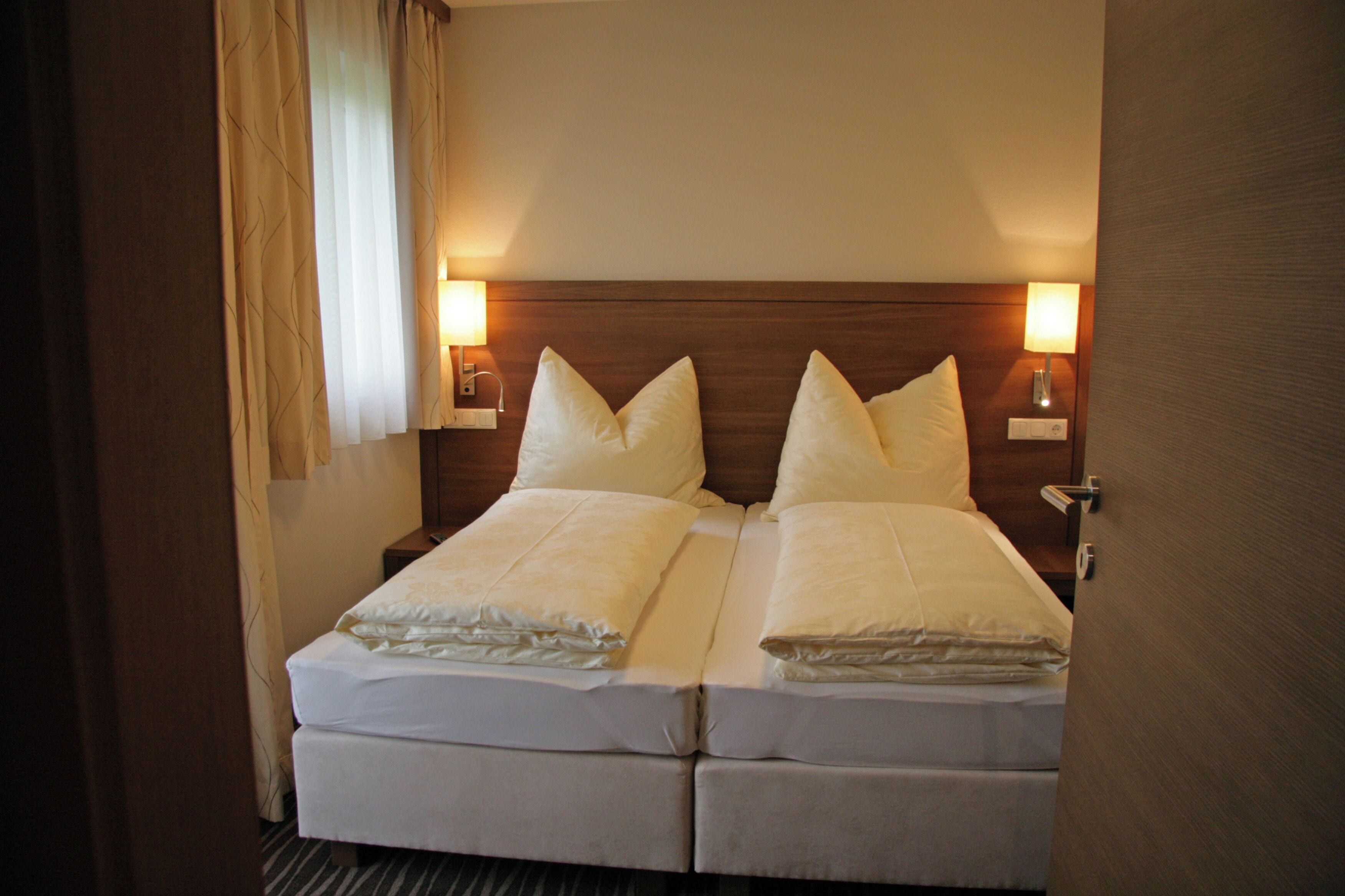 A double bed with two pillows, a wooden headboard, bedside lamps, and a window with curtains.