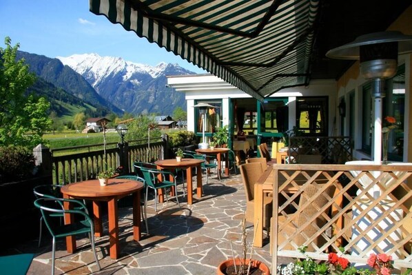 An outdoor patio with tables and chairs, a wooden fence, and a mountain backdrop. - Landhaus Rohregger (Neukirchen am Grossvenediger)