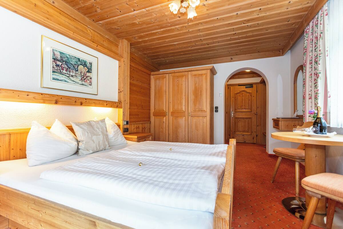 A double bed with a wooden headboard, a wooden wardrobe, and a small table with a chair.