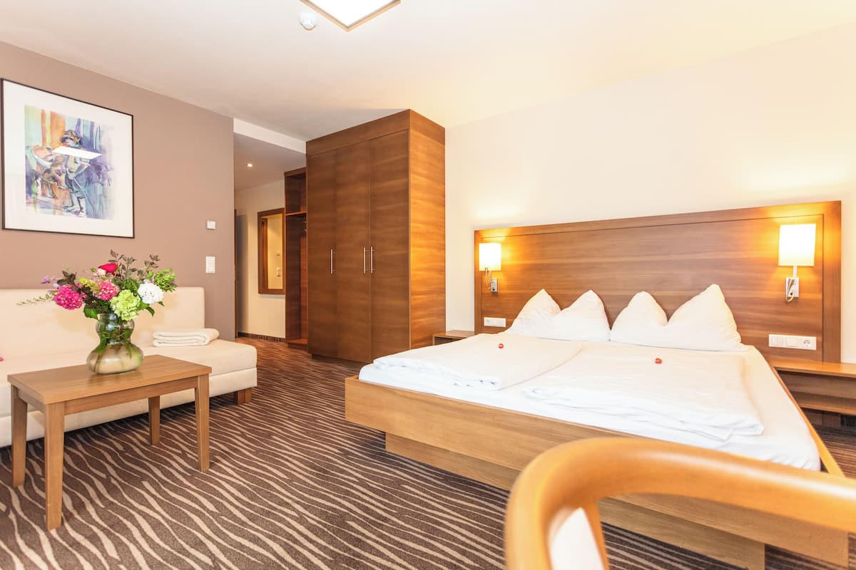 A hotel room with a large bed, a wooden wardrobe, a small table with a vase of flowers, and a painting on the wall.