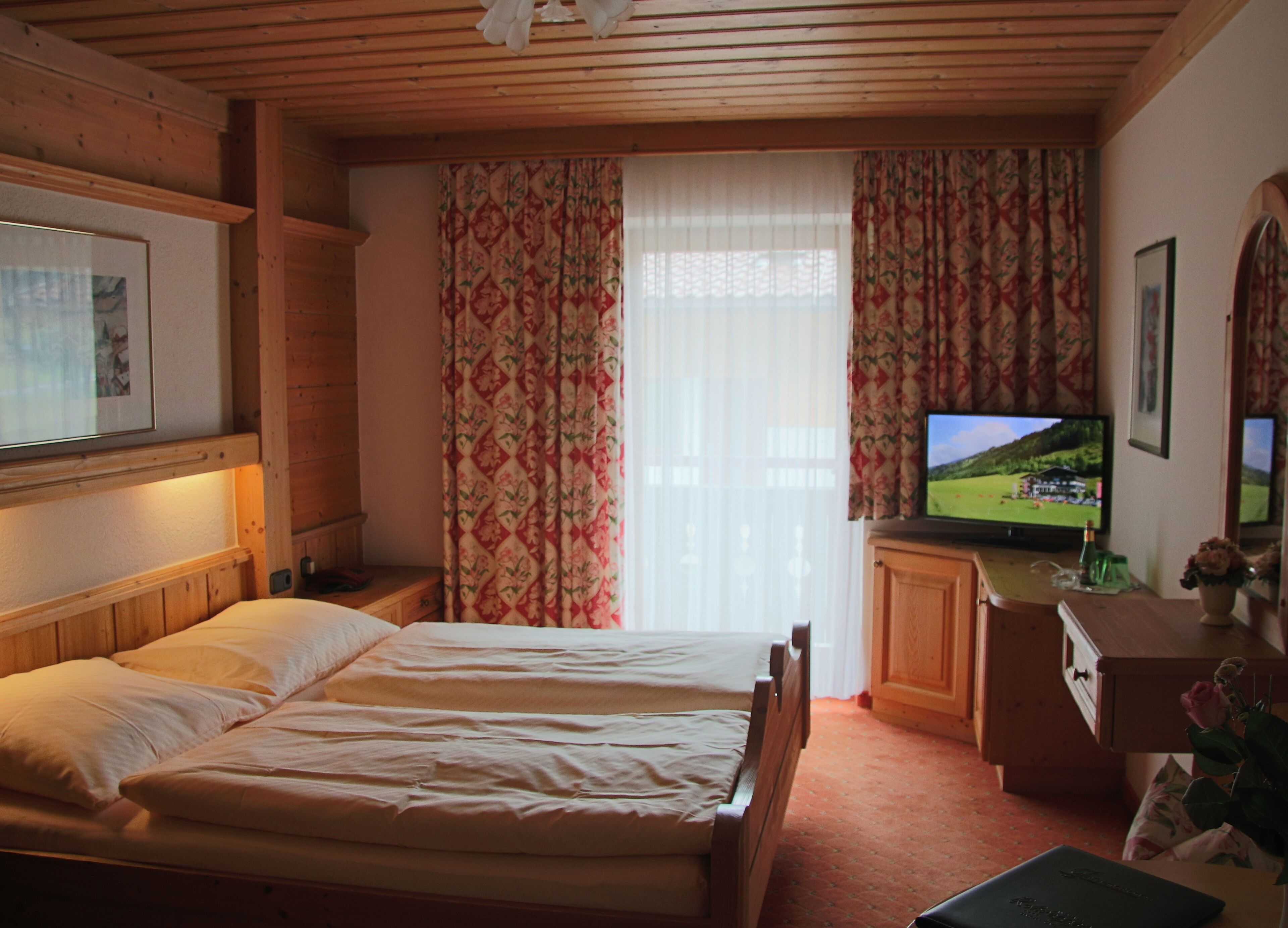 Un dormitorio con dos camas, un televisor, un aparador de madera y una ventana con cortinas florales.