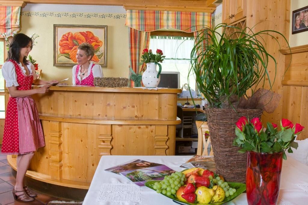 A reception area with a wooden counter, a framed floral painting, and a table with fruit and magazines.