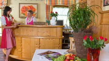 A reception area with a wooden counter, a framed floral painting, and a table with fruit and magazines.