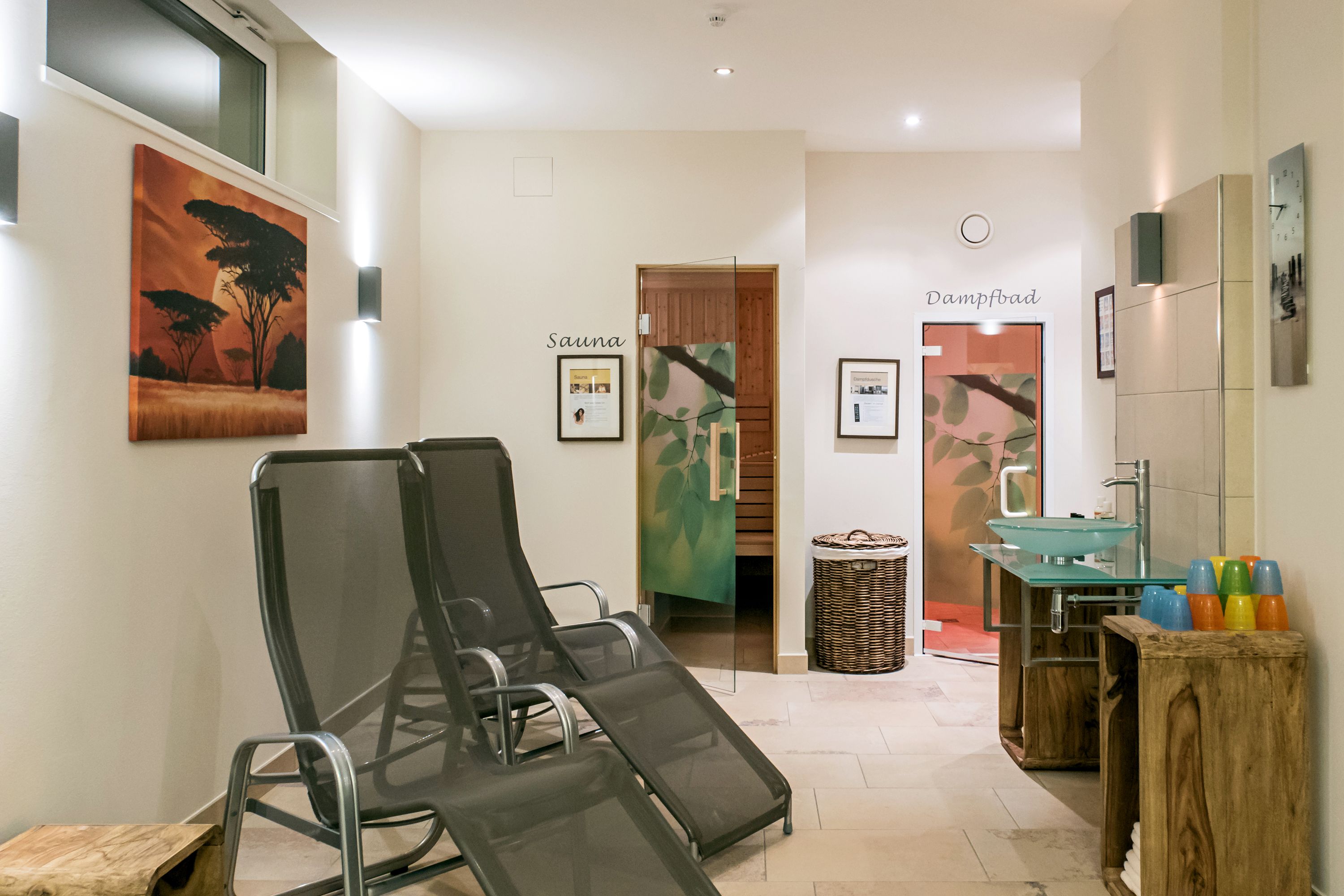 A spa area with a sauna, a massage chair, a sink, and a wooden stool with colorful cups.