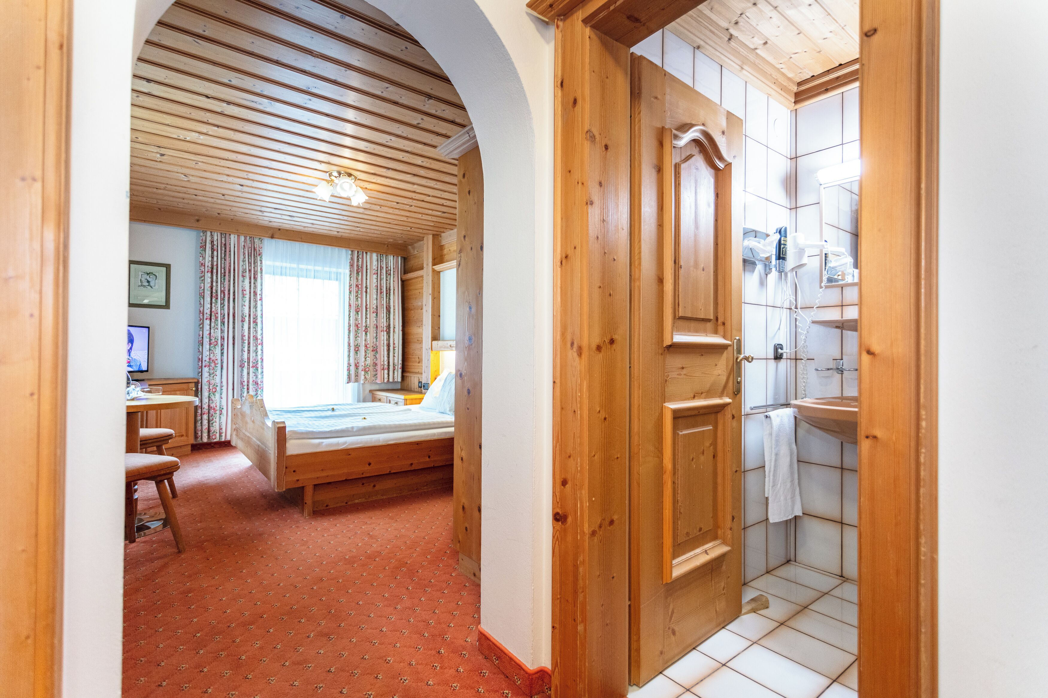 Una habitación de madera con cama, escritorio y baño con lavamanos y espejo.