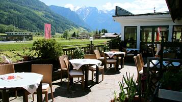 Een terras buiten met rieten meubels en tafels, met uitzicht op een bergachtig landschap.