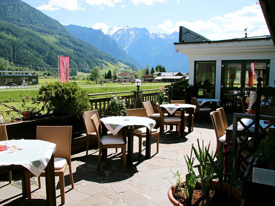 Een terras buiten met rieten meubels en tafels, met uitzicht op een bergachtig landschap.