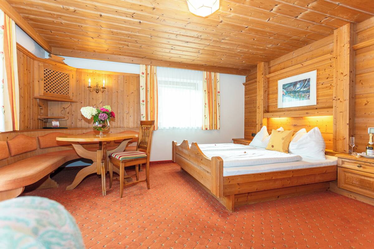 A wooden cabin-style room with a bed, a wooden bench, a table, and a chair.
