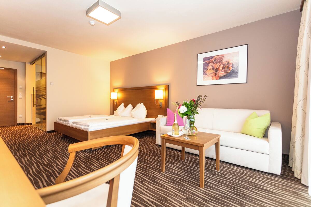 A hotel room with a bed, a sofa, a coffee table, and a painting on the wall.