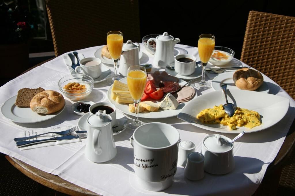 Una mesa de desayuno con platos de huevos, tostadas y fruta, acompañada de café y jugo de naranja.