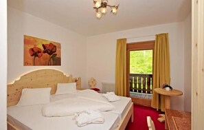 Une chambre d’hôtel avec une tête de lit en bois, un tableau représentant des fleurs, une fenêtre avec des rideaux et une petite table sur laquelle est posée une plante.