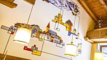 Eine Decke mit einem farbenfrohen, geometrischen Design, das Gebäude und hängende Lampen zeigt.