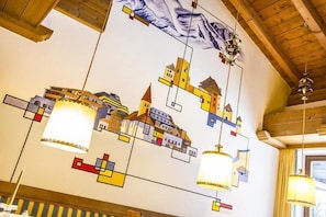 Un plafond orné d’un motif géométrique coloré représentant des bâtiments et des lampes suspendues.