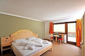 Une chambre à coucher avec un lit en bois, une petite table avec une chaise et une fenêtre avec des rideaux.