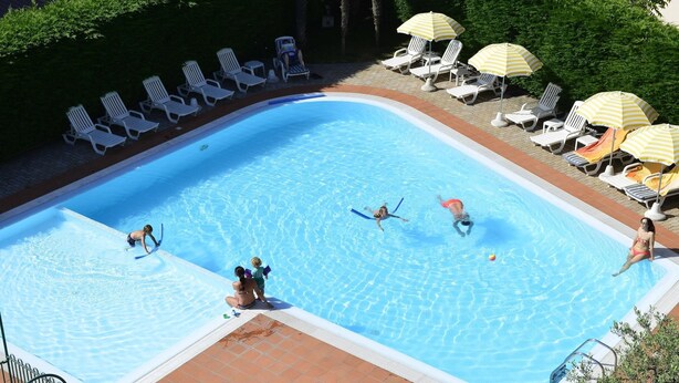 Une piscine dotée de plusieurs couloirs, entourée de chaises longues blanches et de parasols jaunes.