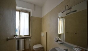 Une petite salle de bain avec des toilettes, un lavabo et un miroir. Il y a une fenêtre avec des rideaux et un radiateur.