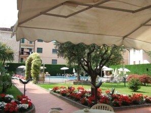Un espace extérieur aménagé avec une terrasse couverte, entouré de parterres de fleurs et d’une pelouse bien entretenue.